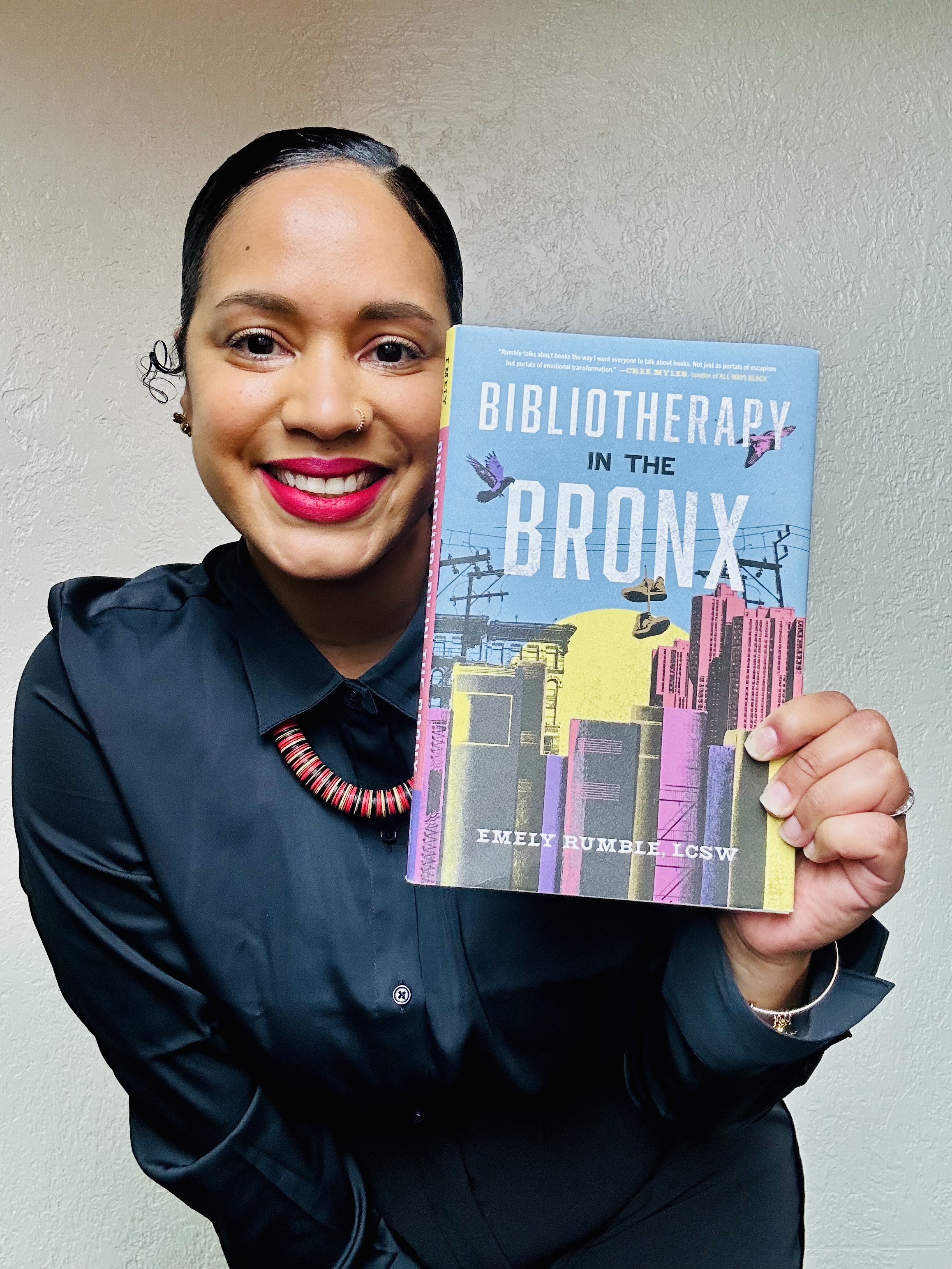 A photo of Emely joyfully holding up a copy of 'Bibliotherapy in the Bronx'